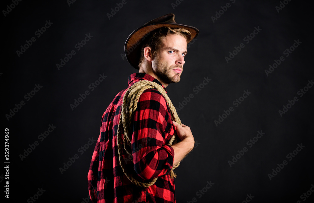 Western life. Man wearing hat hold rope. Lasso tool of American cowboy. Lasso is used in rodeos as part of competitive events. Man unshaven cowboy black background. Lasso can be tied or wrapped