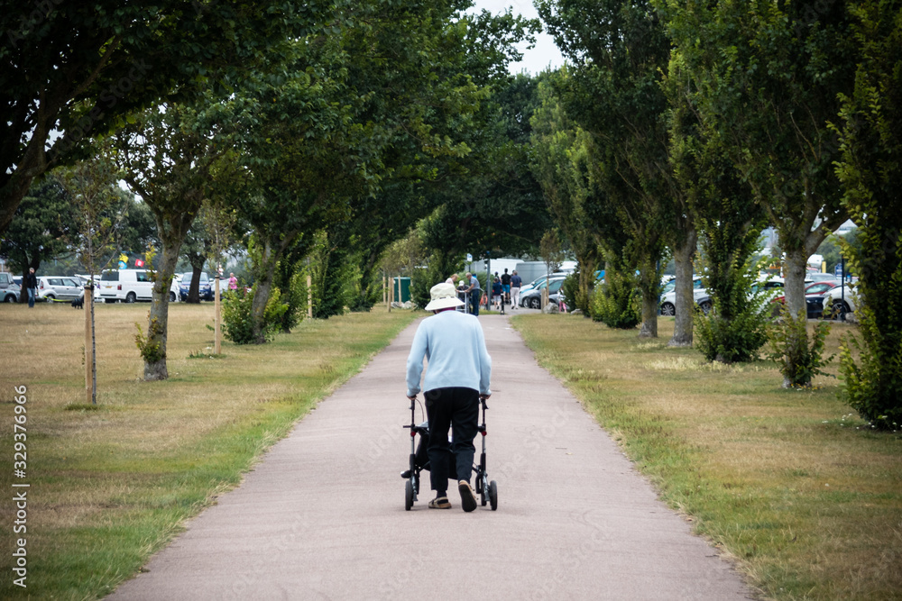 an elderly lady walking the a park using a walking aid or mobility aid