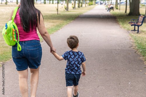 A mother walking through a park with her son holding hands