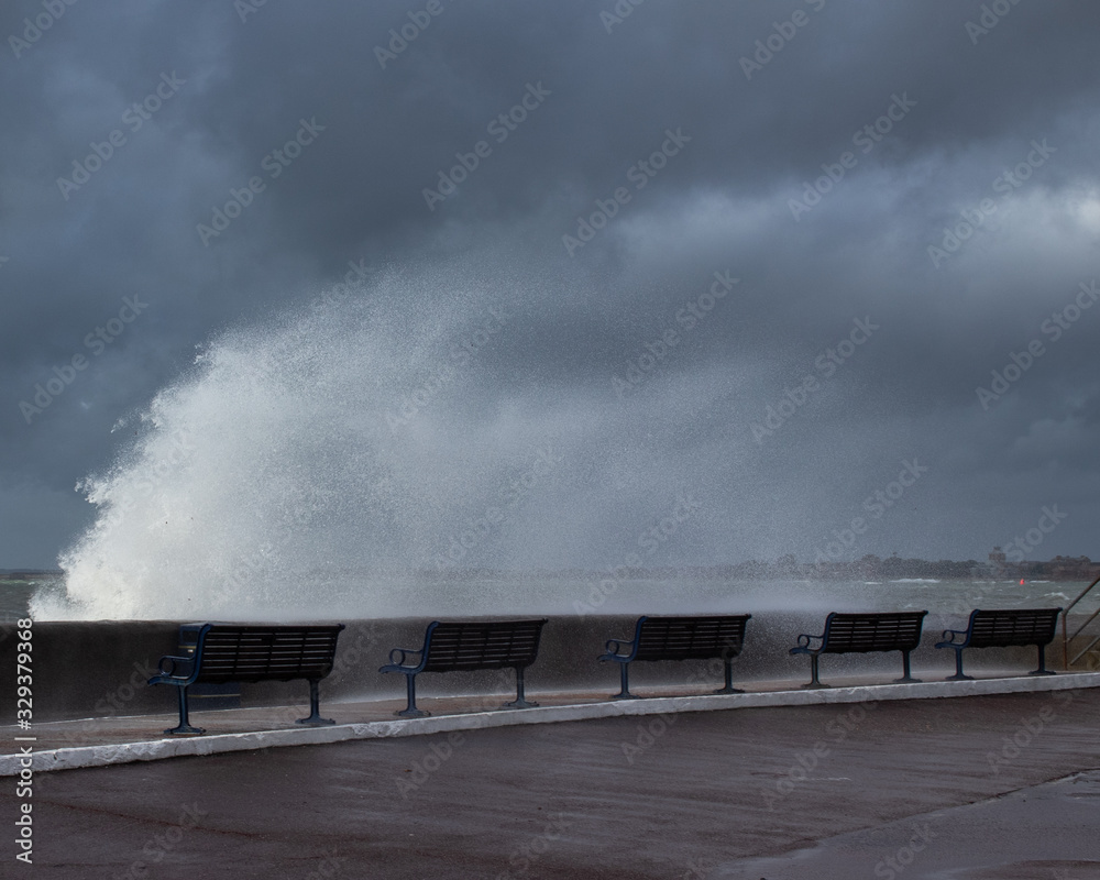 waves breaking over over the seawall and benches during a storm waves breaking over over the seawall and benches during a storm