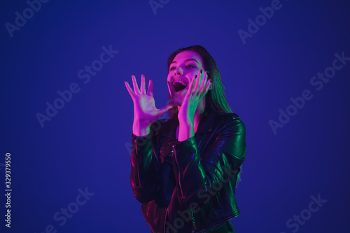 Calling for sales. Caucasian woman's portrait isolated on blue studio background in neon light. Beautiful female model. Concept of human emotions, facial expression, sales, ad. Trendy colors.