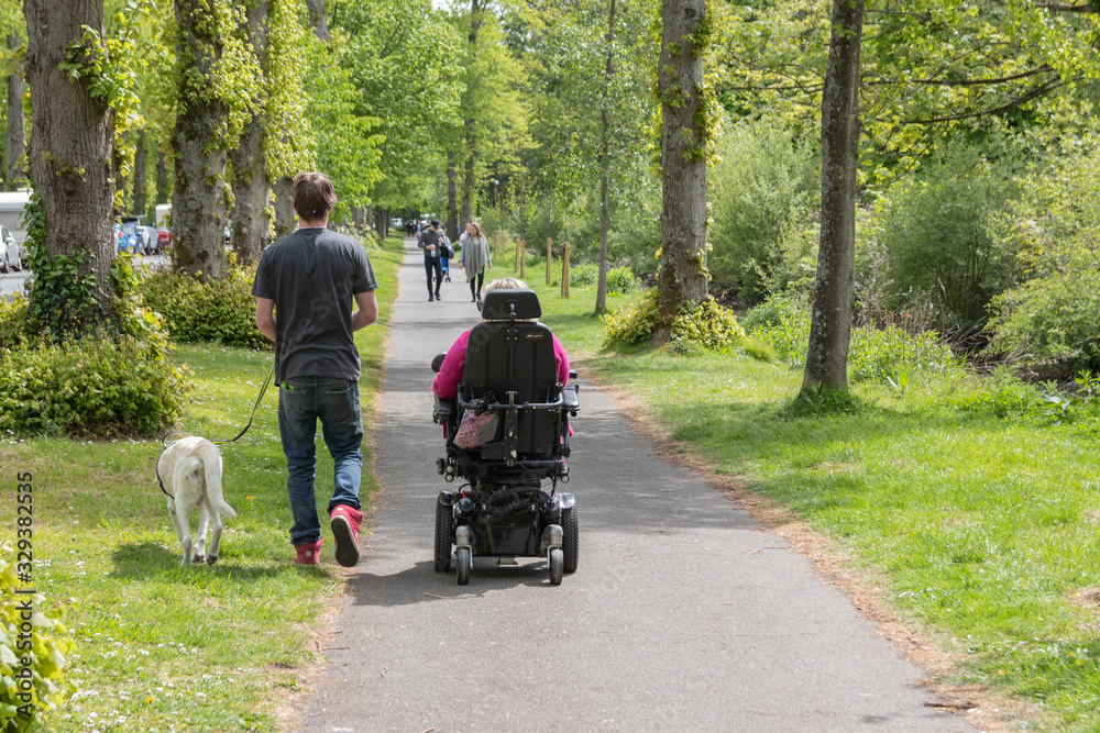 a woman in an electric scooter with her carer walking next to her with a support dog a woman in an electric scooter with her carer walking next to her with a support dog