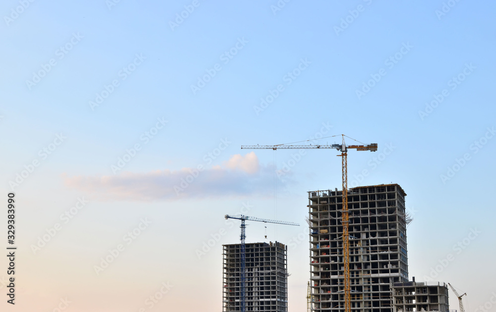 Tower cranes and new residential high-rise buildings at a huge construction site on sunset background. Building construction, installation of formwork and concrete structures