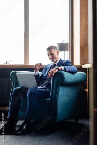 smiling businessman in suit showing yes gesture and using laptop