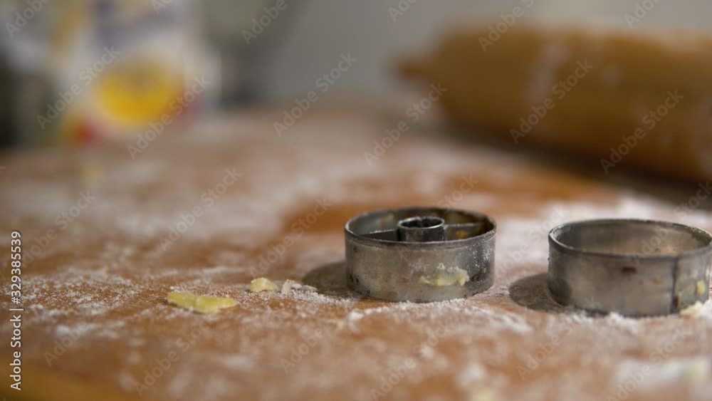 A close detail of cookie cutters and a roller on a table covered with a baking mix. A close detail of cookie cutters and a roller on a table covered with a baking mix.
