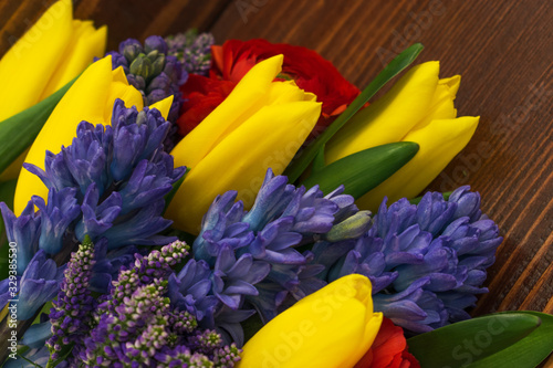 Bright spring bouquet of yellow tulips blue hyacinths speedwell and red ranunculus lying on the brown wooden table.Present concept for Birthday  mother s Day  8 March.Selective focus