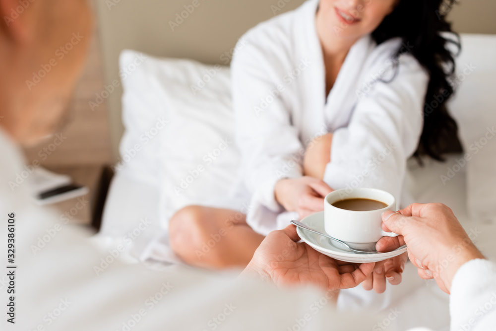 cropped view of boyfriend giving cup of coffee to smiling girlfriend in hotel