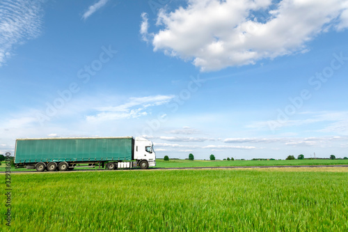 Transportation truck driving on the road, green meadow with blue sky