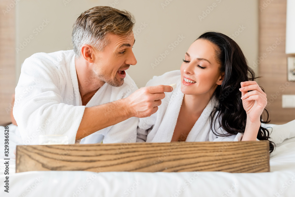 smiling boyfriend feeding attractive girlfriend with cheese in hotel