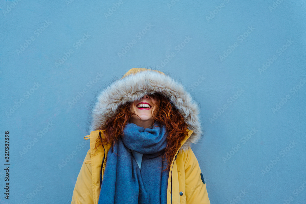 Female isolated on blue background with copy space. Bright complementary colors. Travel and winter holidays concept. Cheerful woman looking up with a hood winter yellow coat about to sneeze. Female isolated on blue background with copy space. Bright complementary colors. Travel and winter holidays concept. Cheerful woman looking up with a hood winter yellow coat about to sneeze.