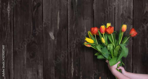The spring sale. A bouquet of fresh red and yellow tulips in the girl 's hand on a rustic wooden background.Mothers and women's day.Spring festival.Banner for a store or website.Zero Waste.Copy space