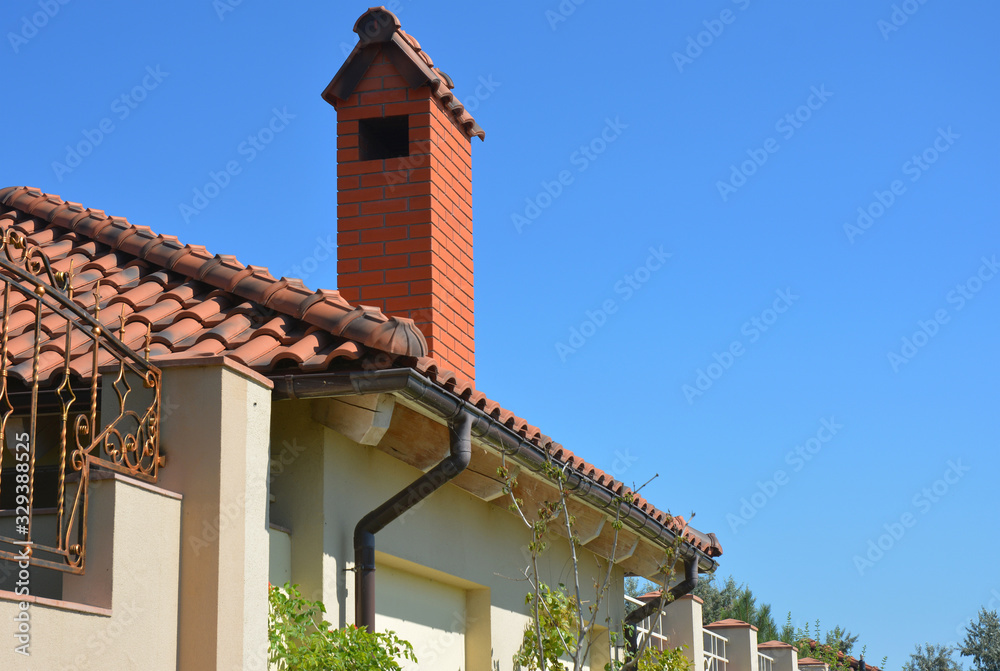 A facade of a modern house with clay tiles rooftop, red brick chimney, and roof gutters. A facade of a modern house with clay tiles rooftop, red brick chimney, and roof gutters.