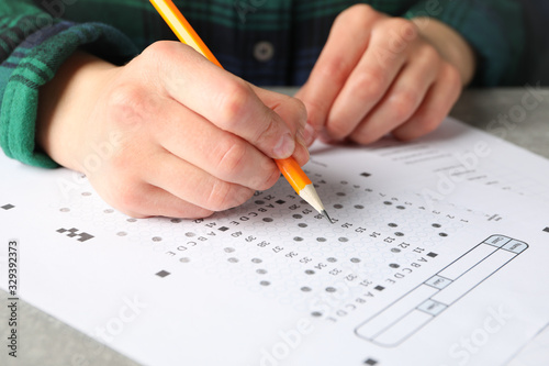 Young woman fills test sheet on grey table, close up