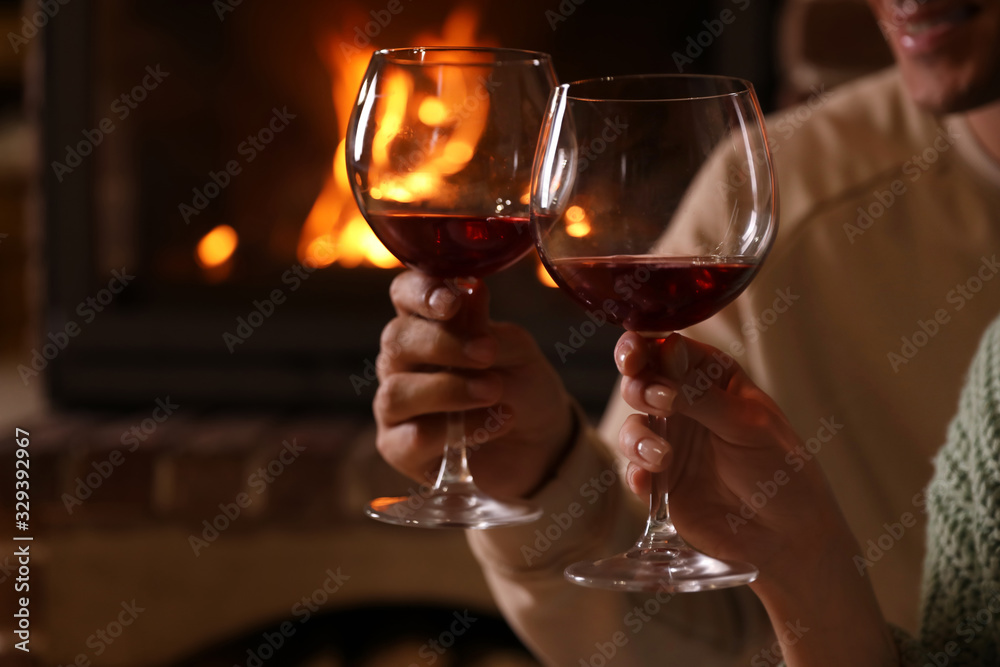 Lovely couple with glasses of wine near fireplace indoors, closeup. Winter vacation Lovely couple with glasses of wine near fireplace indoors, closeup. Winter vacation
