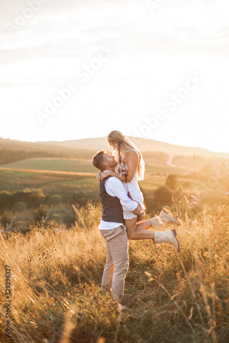 Shot of young boho hippie woman being carried by her handsome boyfriend in summer field. Couple having fun on their summer evening outdoors © sofiko14