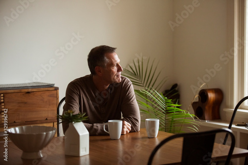 Thoughtful mature man looking away while sitting at table in living room