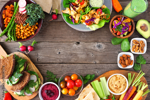 Healthy lunch food frame. Table scene with nutritious Buddha bowl, lettuce wraps, sandwiches, salad and vegetables. Overhead view over a rustic wood background. Copy space.