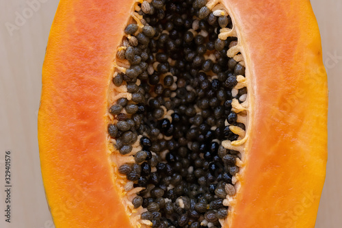 Tropical papaya fruit of orange color in a cut form with black seeds on an isolated wooden light background. Raw fruits healthy food. Diet. Veganism and vegetarianism.