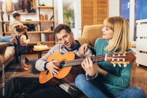 Romantic couple having fun at home, man playing guitar, child in background.