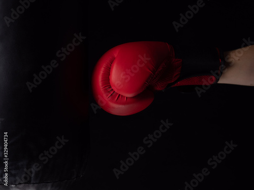 red boxing glove hitting the punching bag on black background © Milos