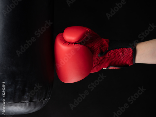 red boxing glove hitting the punching bag on black background © Milos