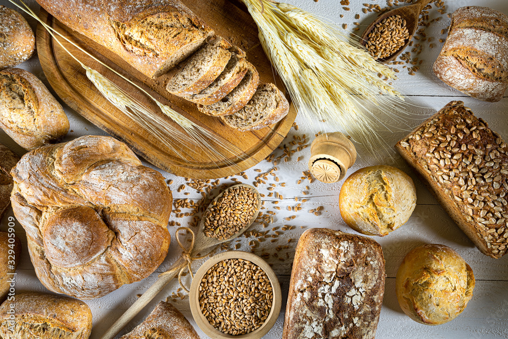 Traditional wheat bread, rolls and ears of cereals on a white wooden background