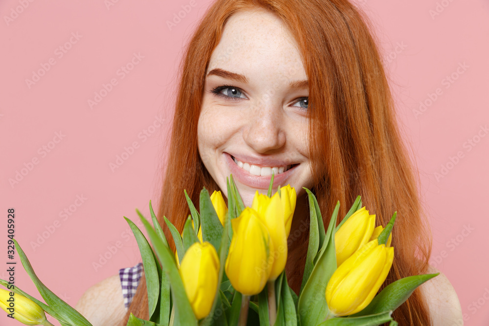 Close up of smiling young redhead woman girl in plaid dress posing isolated on pastel pink wall background studio portrait. People lifestyle concept. Mock up copy space. Hold bouquet of yellow tulips. Close up of smiling young redhead woman girl in plaid dress posing isolated on pastel pink wall background studio portrait. People lifestyle concept. Mock up copy space. Hold bouquet of yellow tulips.