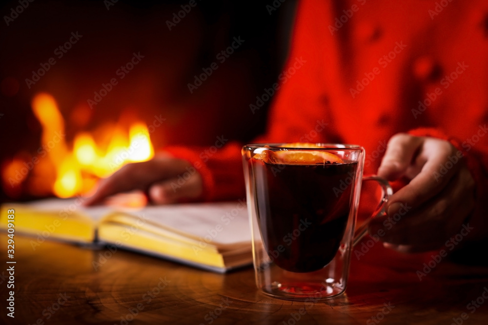 Woman with tasty mulled wine reading book near fireplace at home, closeup Woman with tasty mulled wine reading book near fireplace at home, closeup