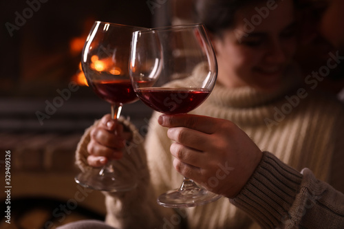 Lovely couple with glasses of wine near fireplace at home, focus on hands. Winter vacation
