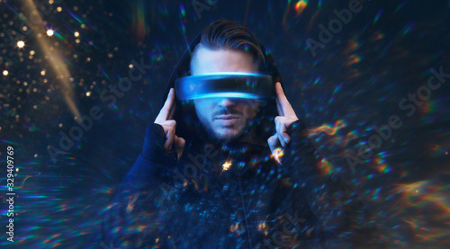 Young man in hoodie on virtual reality background. Guy using VR helmet. Augmented reality, future technology, game concept. Blue neon light. 