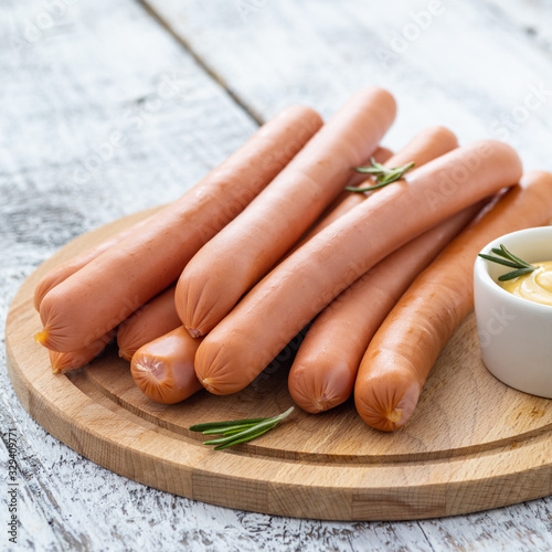 Raw frankfurter sausages with mustard on cutting board.