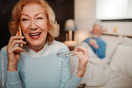 Close shot of smiling blonde elderly woman having a phone call. She is holding her glasses in one hand.