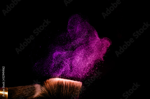 Two make up brushes with flying color powder, product on black background. Concept of glamour make up in minimal black.