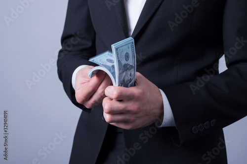 closeup, businessman in a business suit, counts money, holding a press with dollar bills in his hand. On a gray background