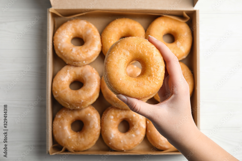 Woman holding delicious donut at white wooden table, top view