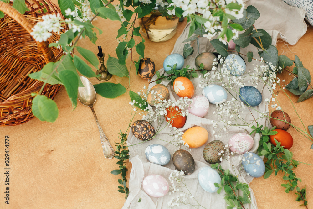 Easter eggs on rustic background with basket, candle, spring flowers and green branches. Stylish colorful Easter eggs with modern ornaments painted with natural dye. Rural flat lay Easter eggs on rustic background with basket, candle, spring flowers and green branches. Stylish colorful Easter eggs with modern ornaments painted with natural dye. Rural flat lay