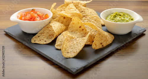 Nachos on a stone plate with two types of sauces, guacamole and tomato cut into small pieces