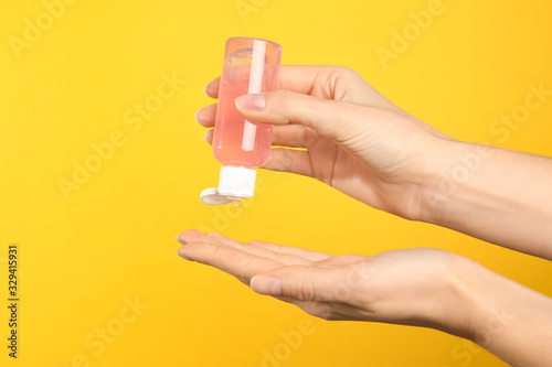 Woman applying antiseptic gel on yellow background, closeup