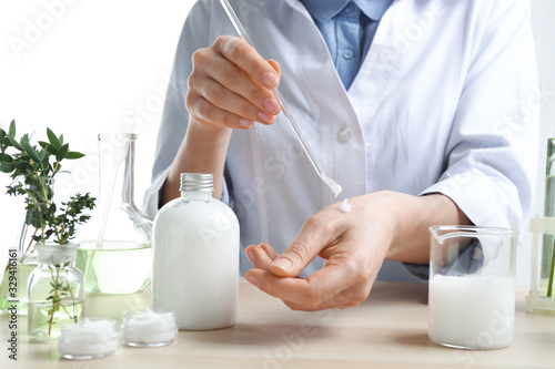 Woman applying natural cream onto hand in cosmetic laboratory, closeup photo