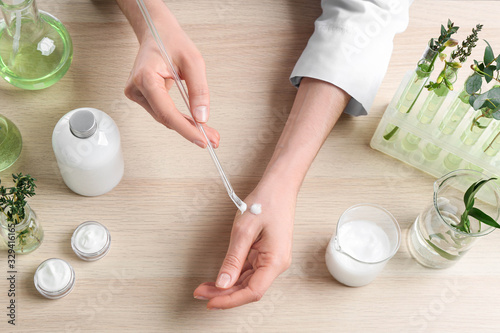 Woman applying natural cream onto hand in cosmetic laboratory, above view