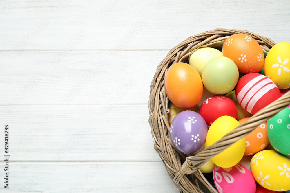 Colorful Easter eggs in basket on white wooden table, top view. Space for text Colorful Easter eggs in basket on white wooden table, top view. Space for text