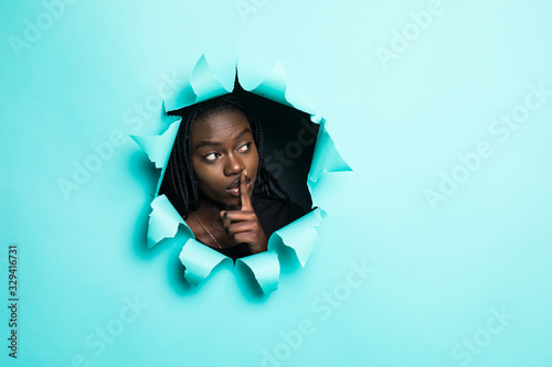 Young afro american woman with silence gesture posing from green paper hole © F8  \ Suport Ukraine