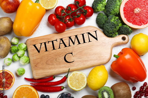 Board with phrase VITAMIN C and fresh products on white wooden table, flat lay