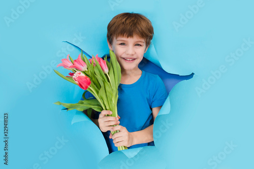 Fun child with bouquet of tulips poses through torn paper hole.  Effect of torn paper. mother's day