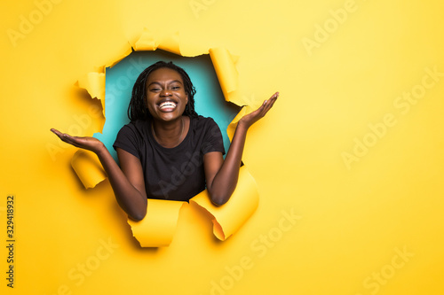 Young african woman confused with raised hands posing from yellow paper hole © F8  \ Suport Ukraine