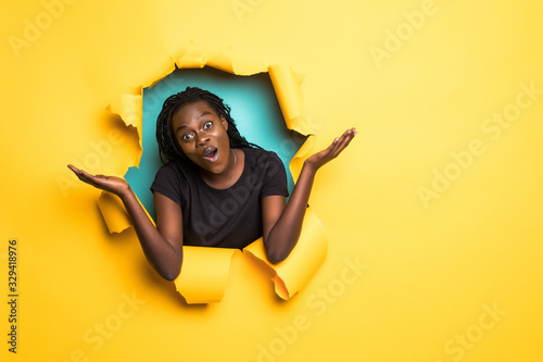 Young african woman confused with raised hands posing from yellow paper hole © F8  \ Suport Ukraine