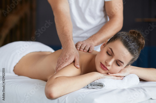 Young beautiful woman enjoying back and shouders massage in spa.Professional massage therapist is treating a female patient in apartment.Relaxation,beauty,body and face treatment concept.Home massage.