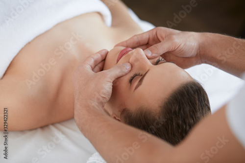 Young beautiful woman enjoying anti-aging facial massage.Male therapist making head massage to female client.Professional masseur.Relaxation,beauty,spa,body and face treatment concept.