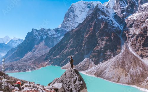 A man standing on the rock in front of turquoise Chola lake and  Tabuche foothills, from the way to Dzongla, Sagarmatha national park, Everest Base Camp 3 Passes Trek, Nepal photo