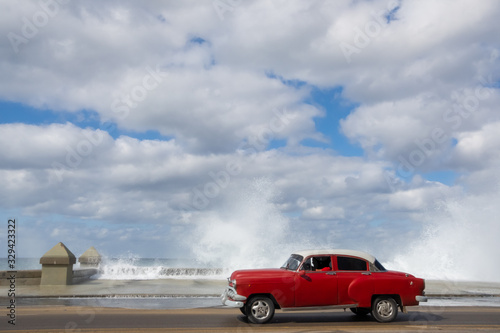 Fototapeta Naklejka Na Ścianę i Meble -  Classic red car driving through the streets of Havana waves splashing